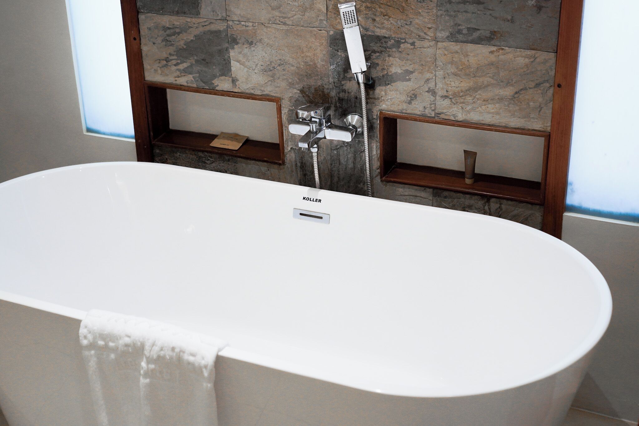 Un baño moderno con una bañera independiente, cabezal de ducha y un muro de piedra de fondo.