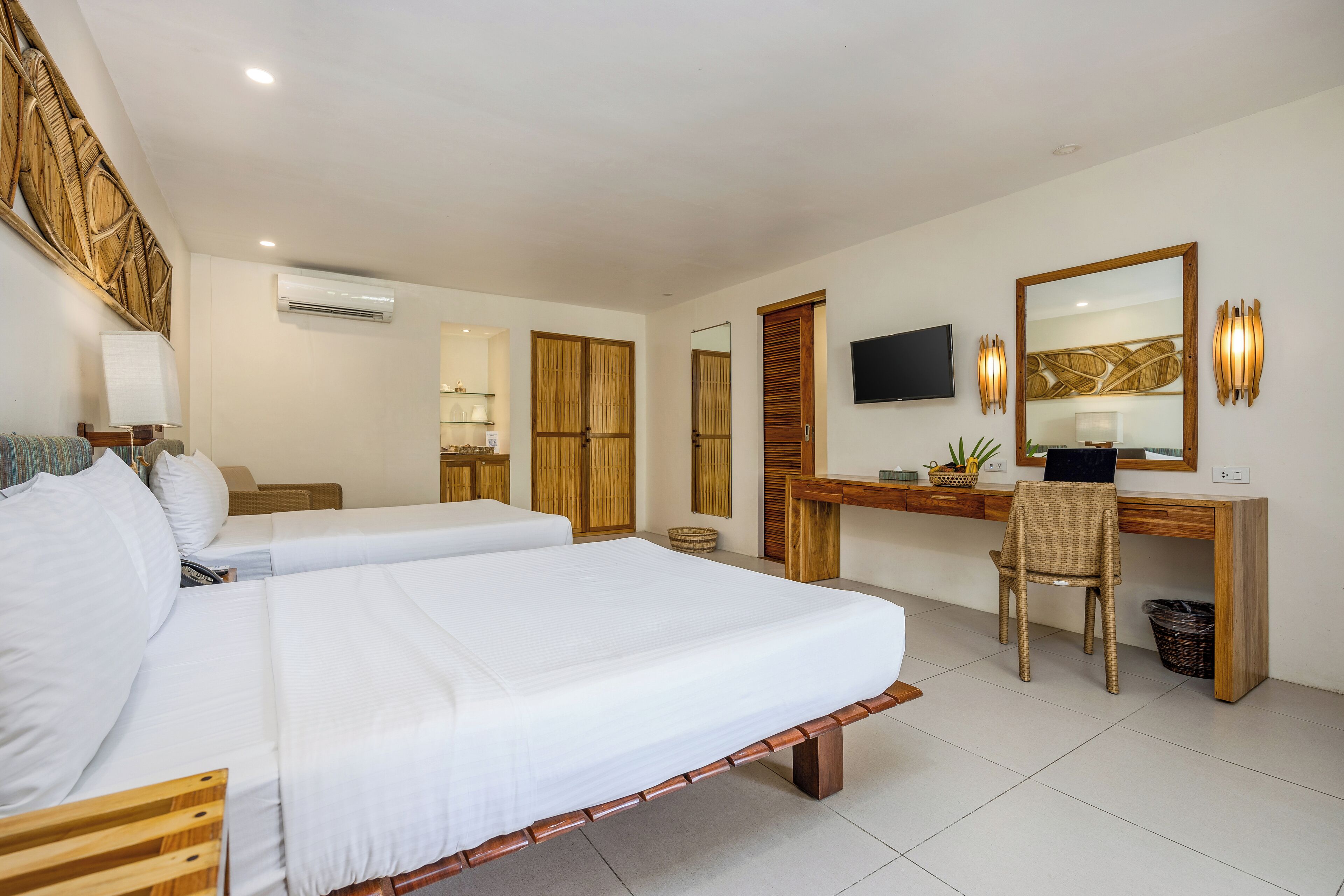 Habitación de hotel con dos camas, un escritorio, una silla, un televisor y un espejo grande.