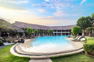 A swimming pool with a curved edge, surrounded by a stone deck and a grassy area.