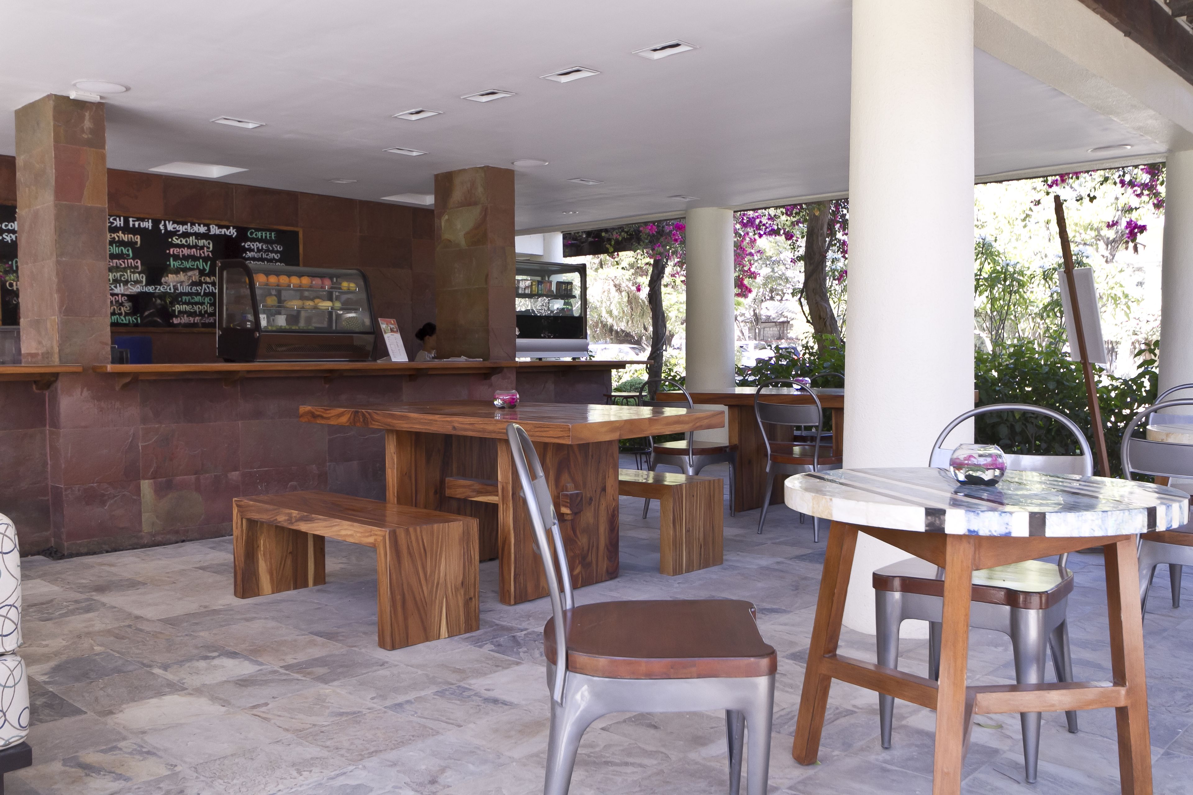 Ein Straßencafé mit Holztischen und -stühlen, einer Kaffeebar inklusive Speisekarte und Blick auf die Straße und Bäume.