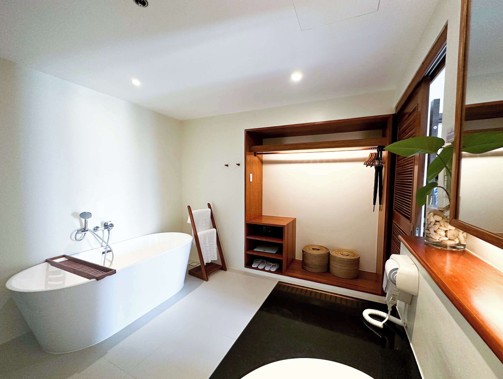 Un baño moderno con una bañera independiente, un perchero, un secador de pelo y una planta pequeña.