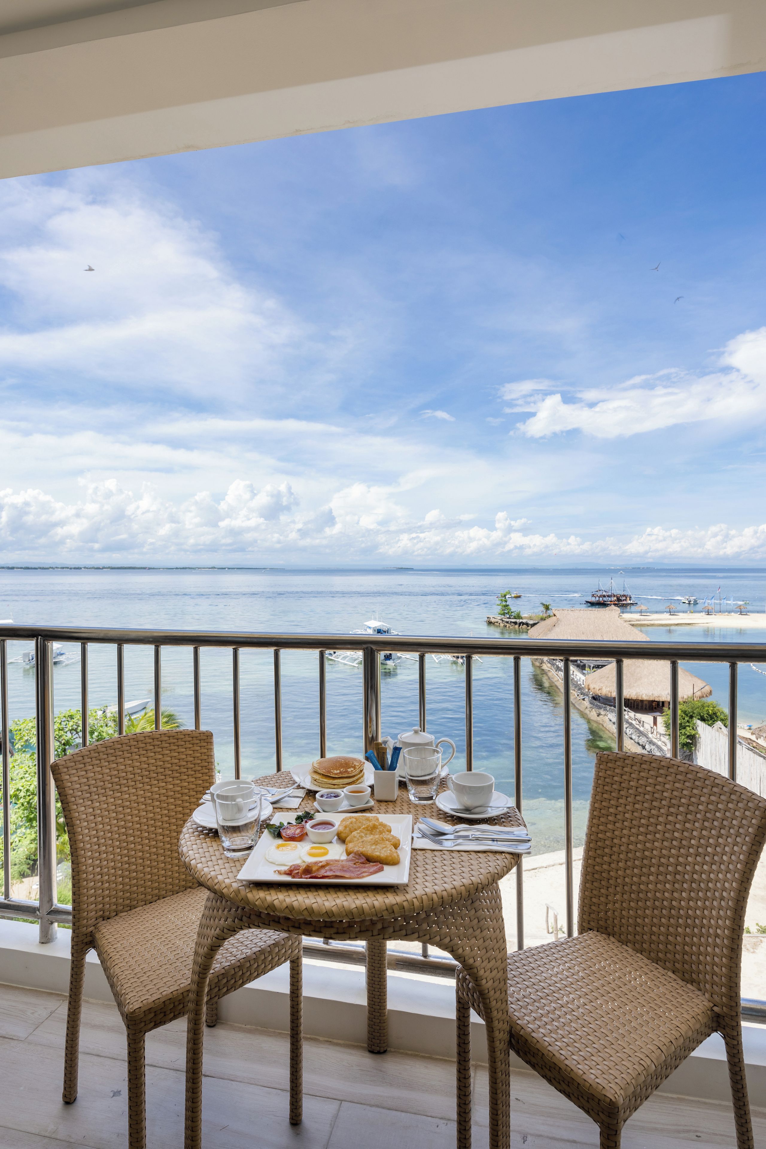 A balcony with a table set for breakfast overlooking a coastal view.