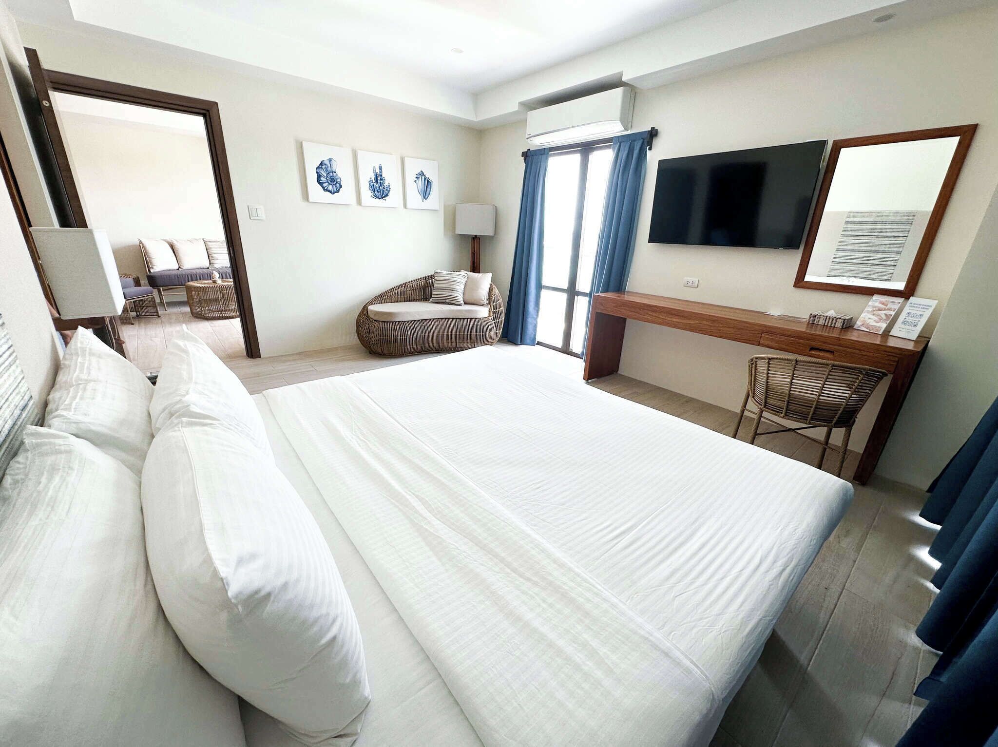 Habitación de hotel con una cama grande, un escritorio, una silla, un televisor y una ventana con cortinas.
