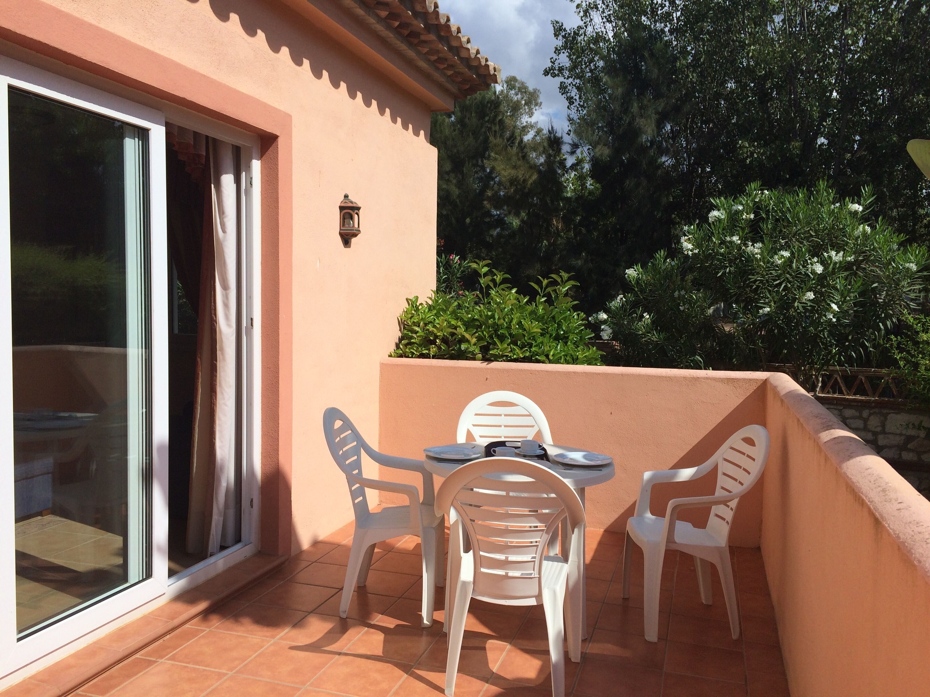 Un patio con una mesa y sillas, una puerta corrediza de vidrio y una pequeña lámpara fijada a la pared.