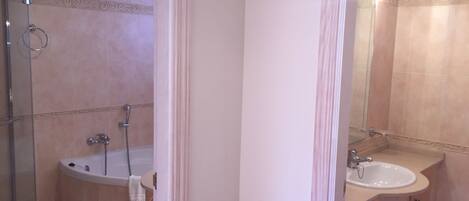 A bathroom with a glass shower enclosure, a bathtub, and a sink with a mirror.