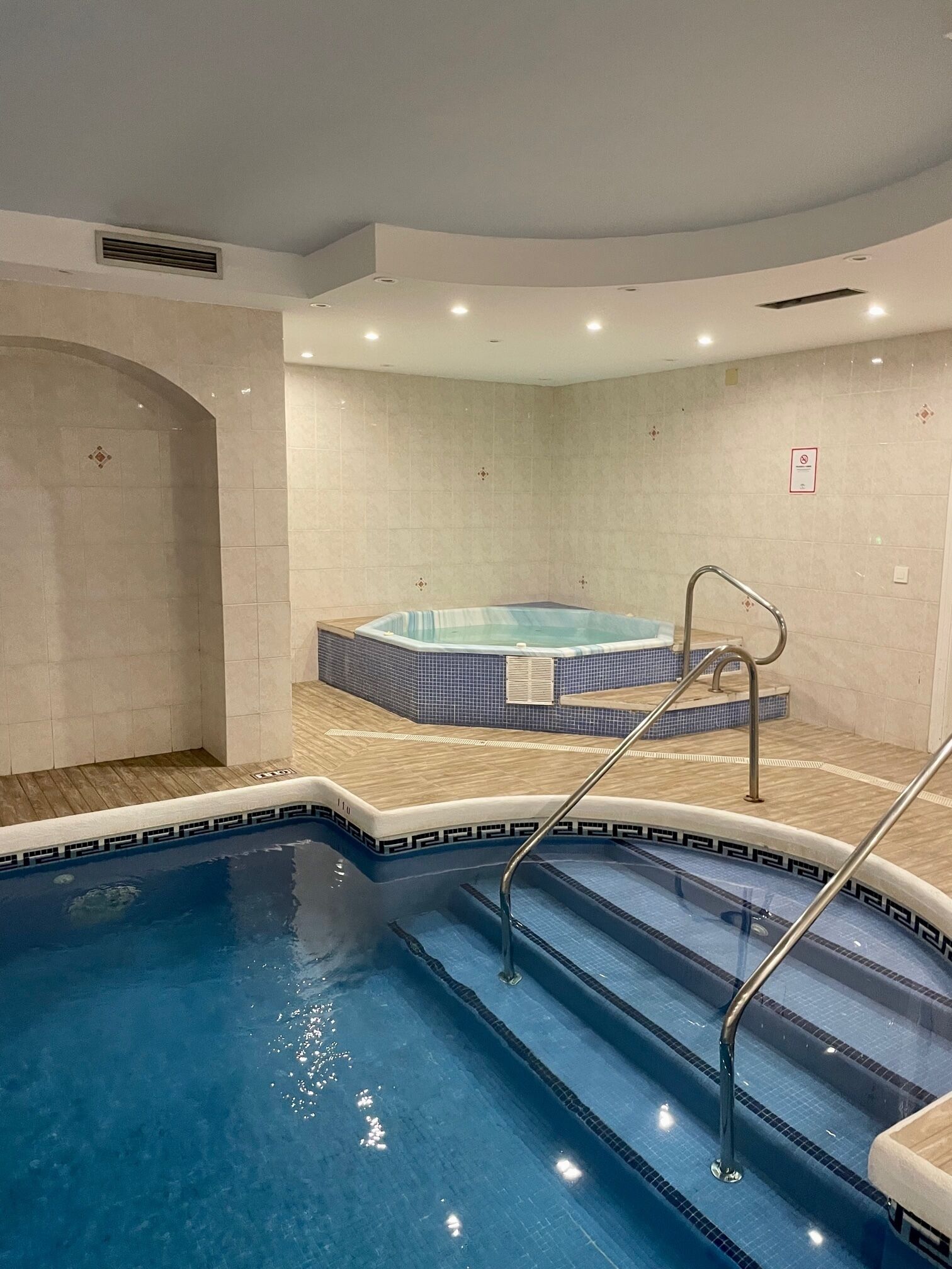 Une piscine avec un jacuzzi, des murs carrelés et un plancher en bois.