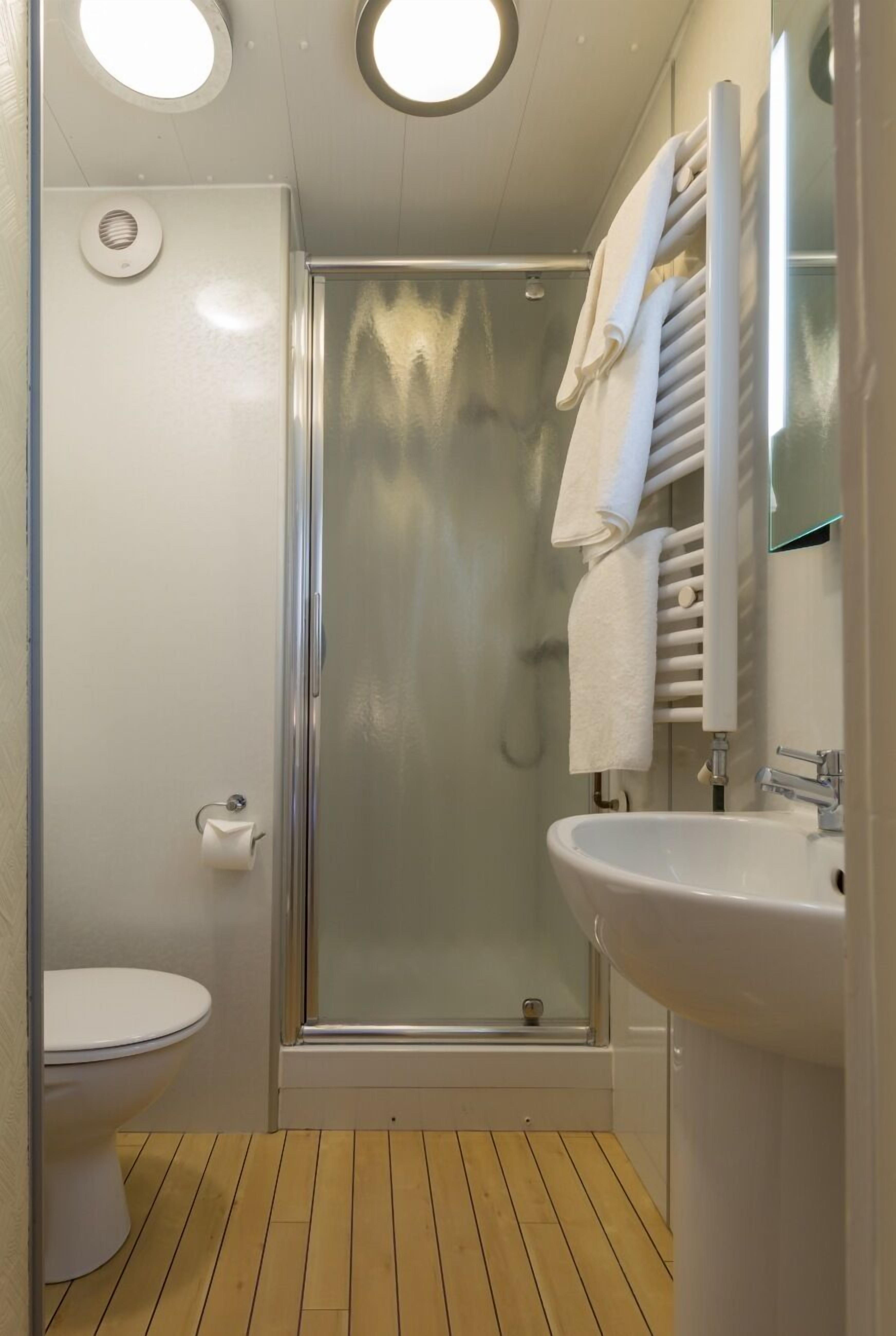 A compact bathroom with a toilet, a glass-enclosed shower, and a sink with a towel rack.