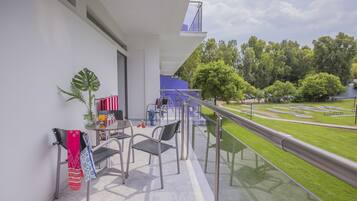 Un balcon doté d’une balustrade en verre, une table avec des chaises et une vue sur une pelouse verdoyante et des arbres.