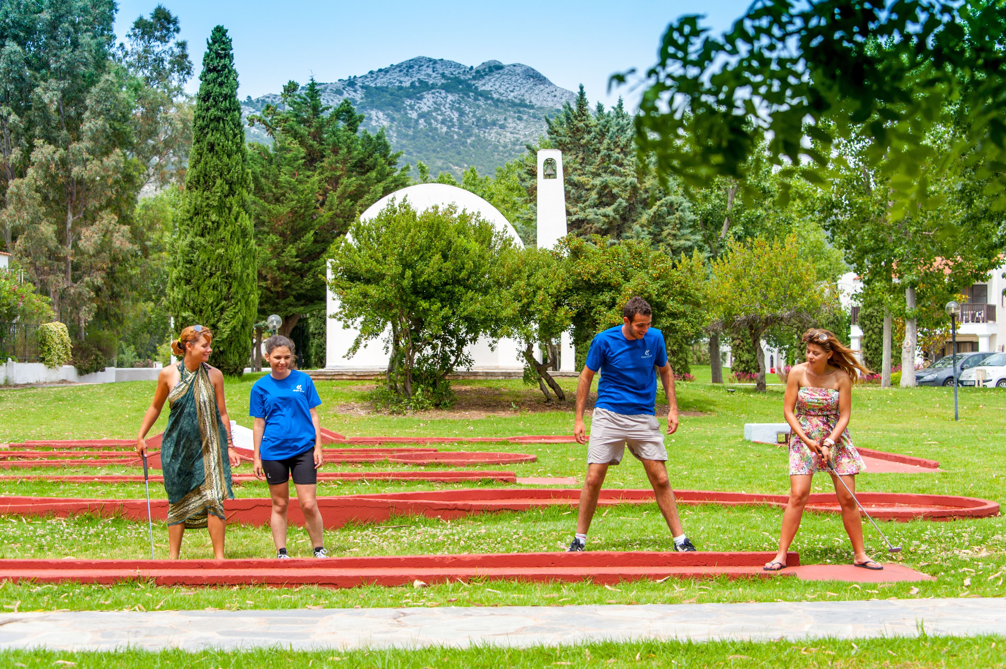 A group of people playing golf in a park with a mountain in the background.