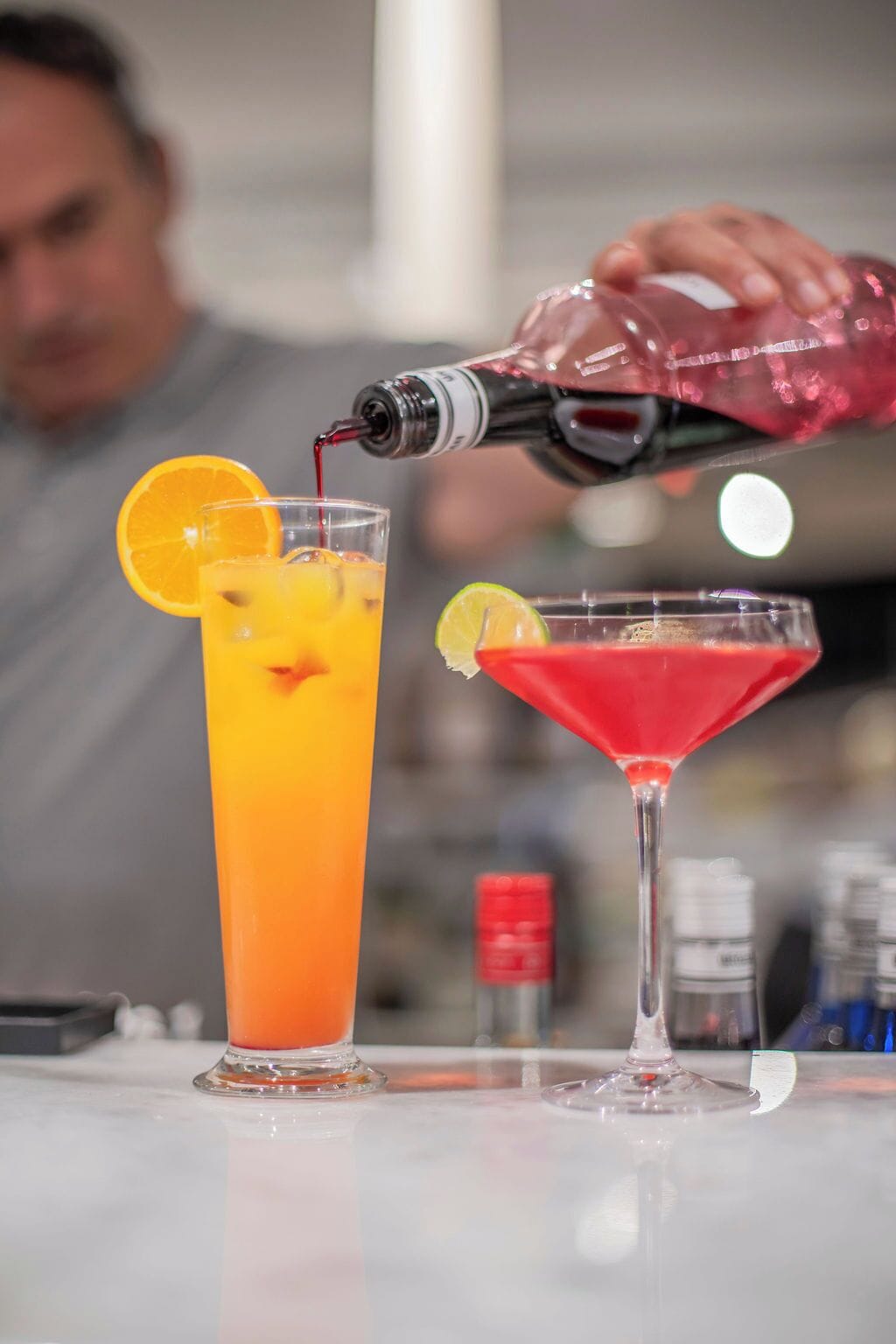 A bartender pouring a drink into a tall glass with an orange slice garnish.