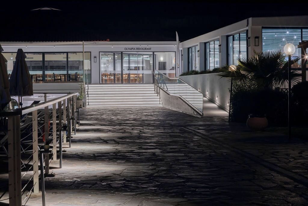 Vue nocturne d’un bâtiment moderne, avec un restaurant appelé « OLYMPIA RESTAURANT » situé à l’entrée.