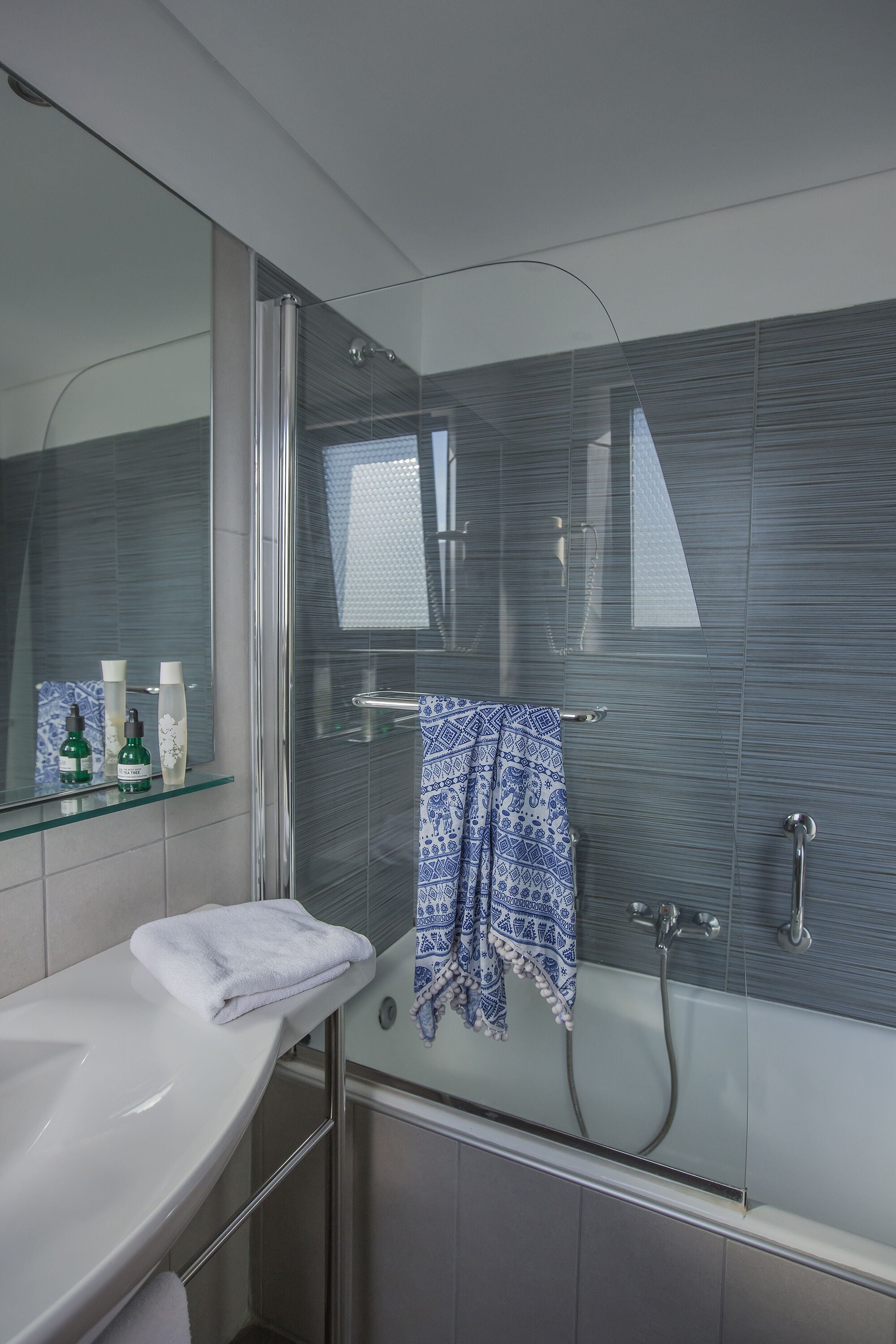 A modern bathroom with a glass shower enclosure, a white sink, and a towel rack with a blue patterned towel.