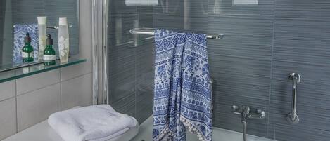 A modern bathroom with a glass shower enclosure, a white sink, and a towel rack with a blue patterned towel.