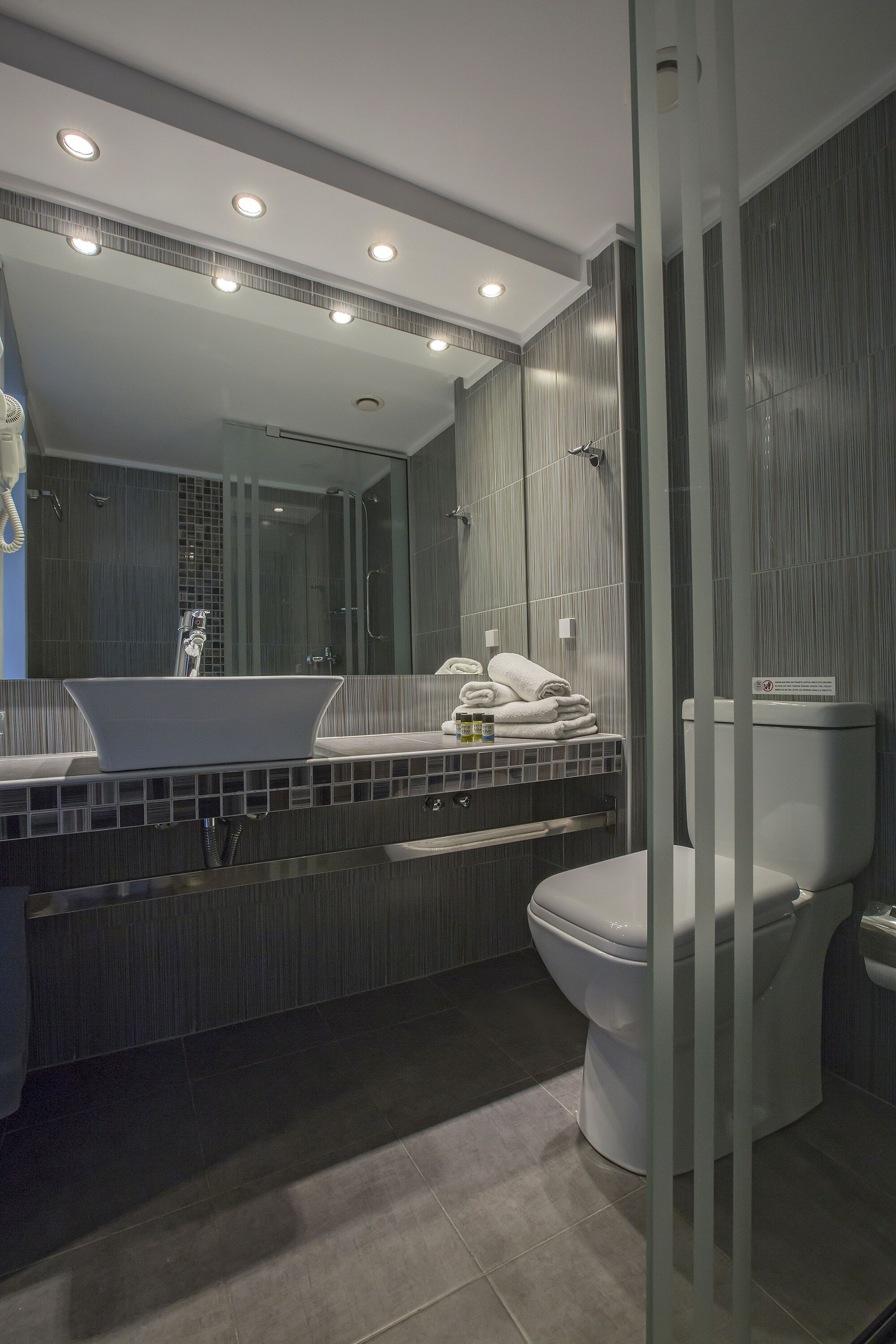 Un baño moderno con un espejo grande, un lavamanos blanco y un inodoro.