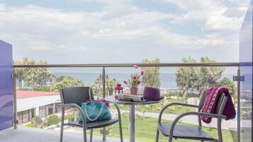 Un balcón con dos sillas, una mesa pequeña con un sombrero y un bolso, y vista al mar y al verdor.