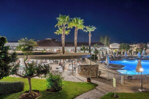 A resort pool area with palm trees, outdoor seating, and a stone structure.