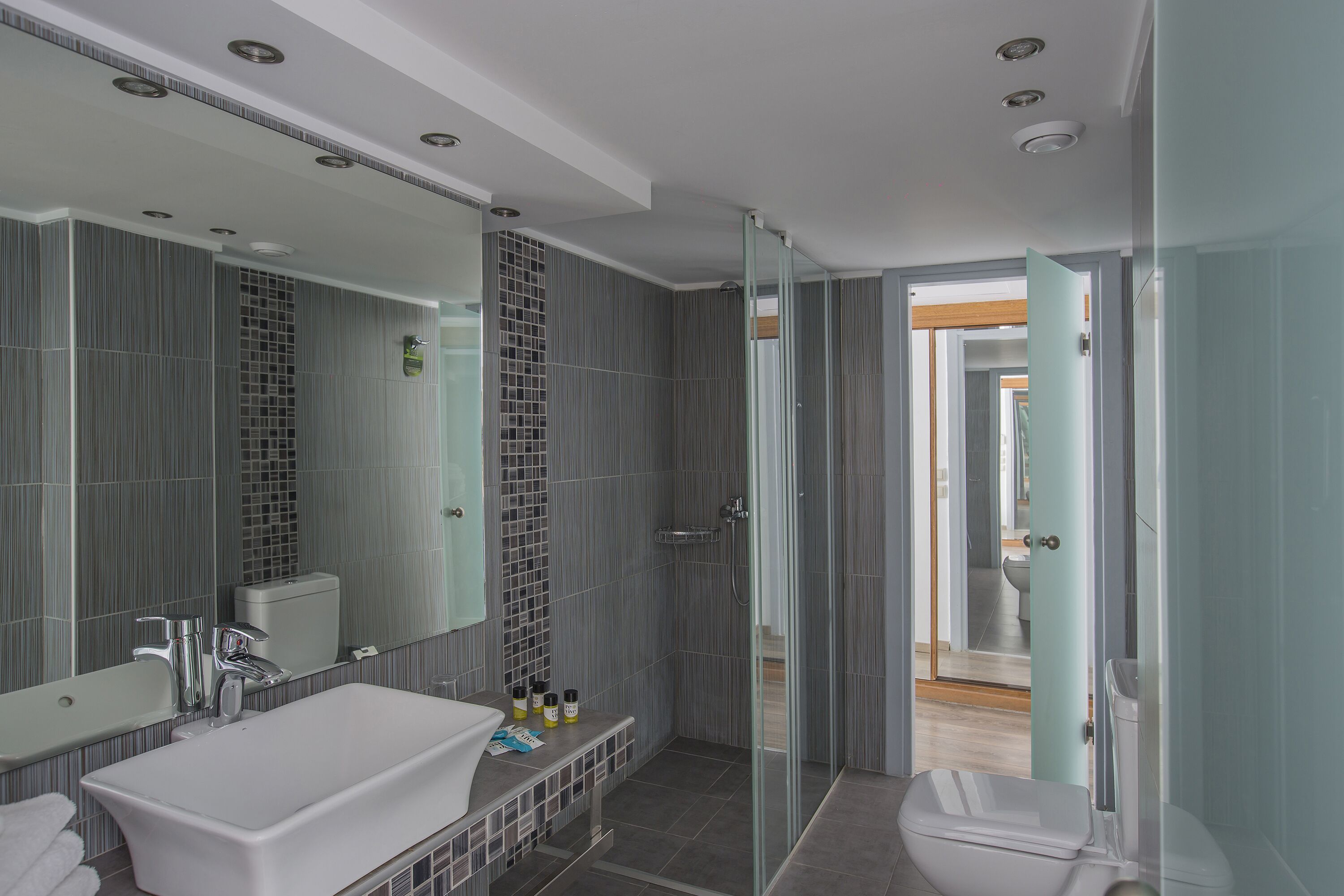 A modern bathroom with a large mirror, a white sink, and a glass-enclosed shower.