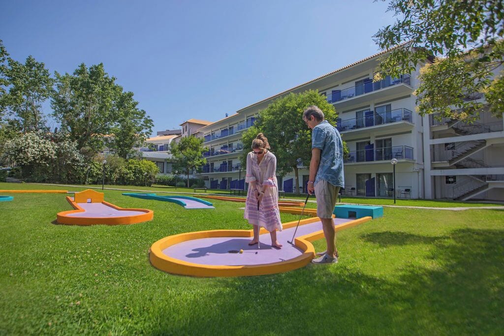 A courtyard with miniature golf holes, a building with balconies, and a clear sky.