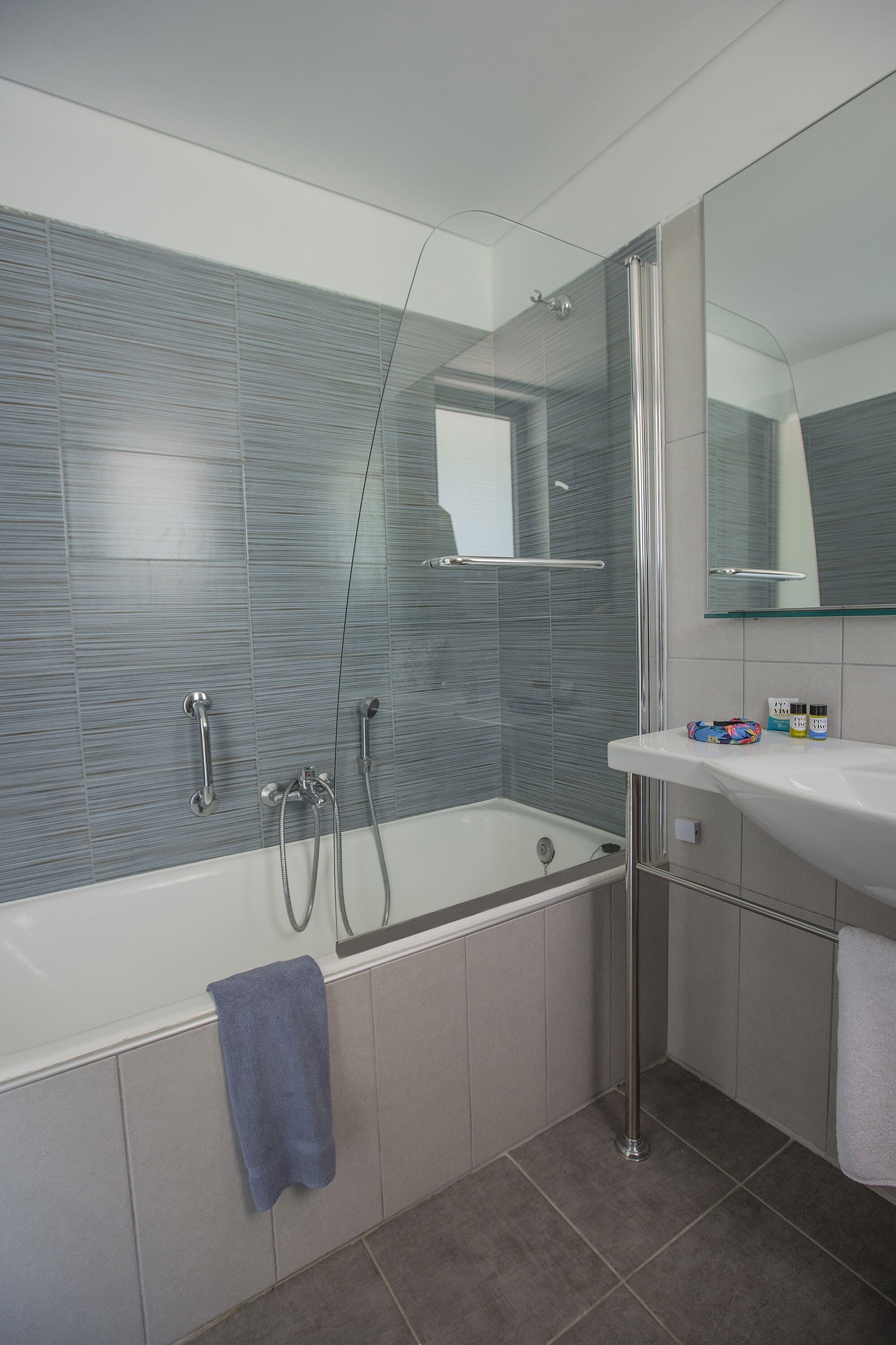 A modern bathroom with a glass shower enclosure, a white bathtub, and a vanity with a mirror.