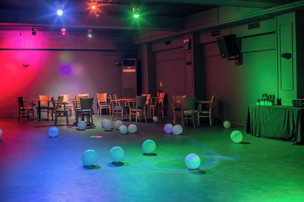 Una habitación con sillas dispuestas en filas, una mesa con botellas y globos en el suelo.