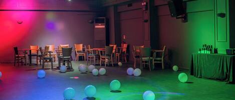 Una habitación con sillas dispuestas en filas, una mesa con botellas y globos en el suelo.