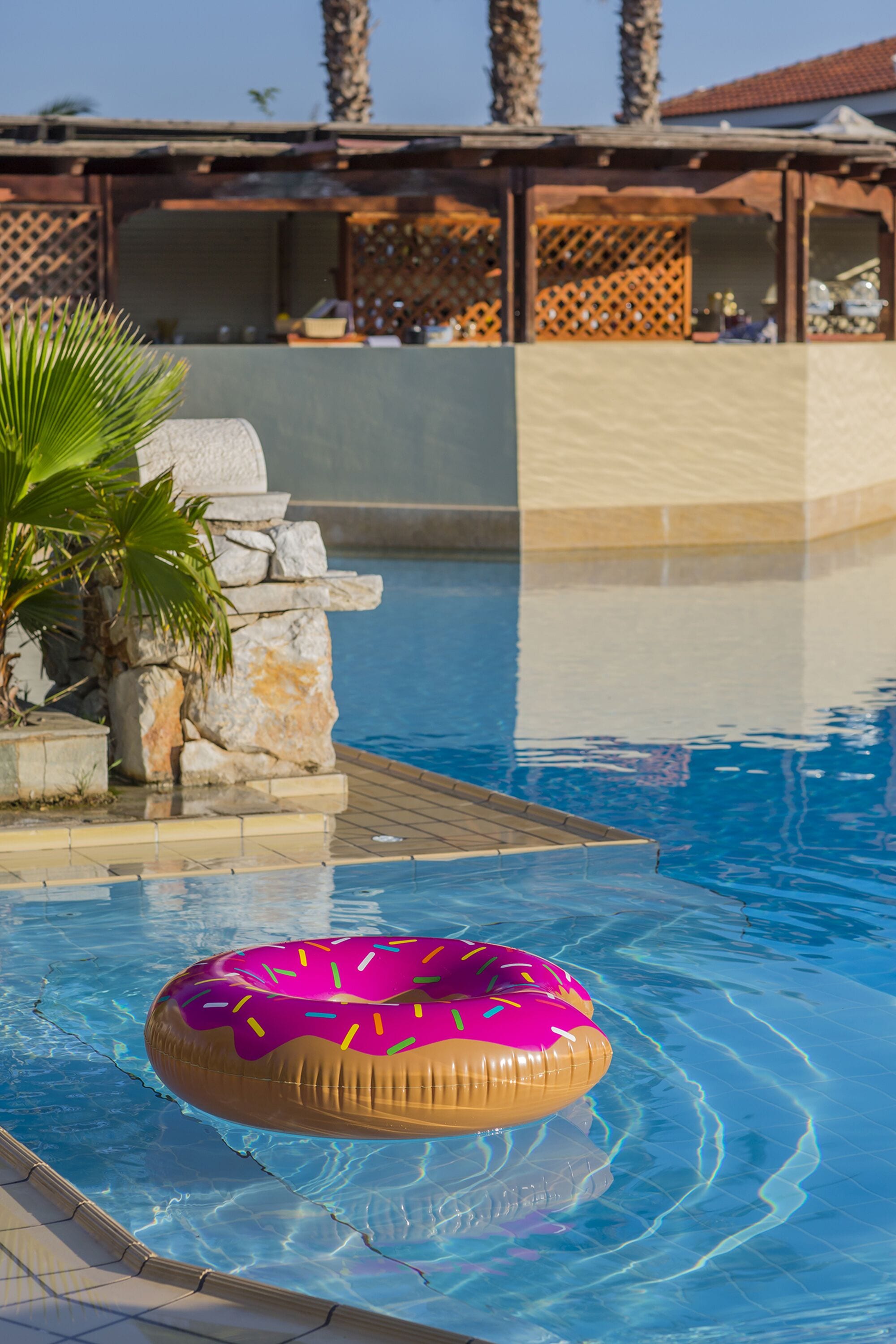 Una piscina con un flotador de rosquilla rosa, una palmera y un muro de piedra.