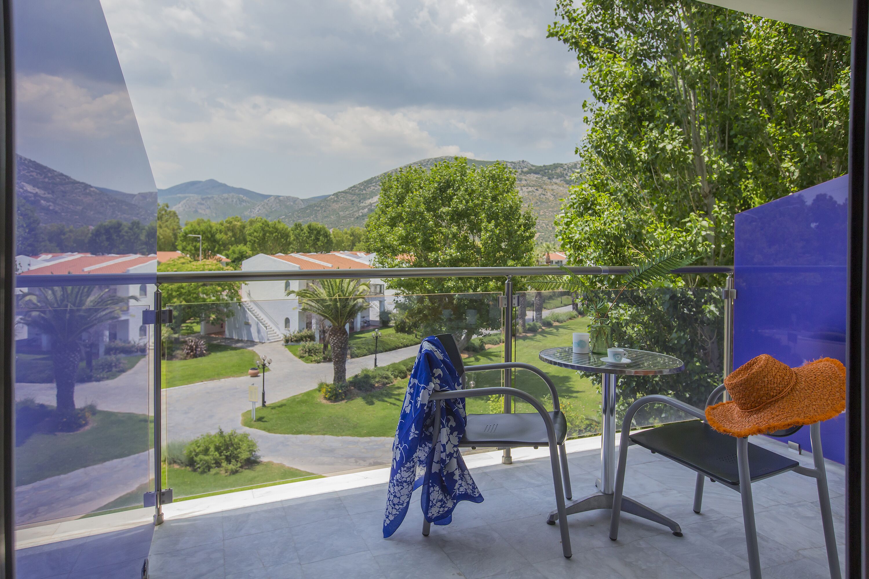 A balcony with a view of a green landscape, a chair, and a table.