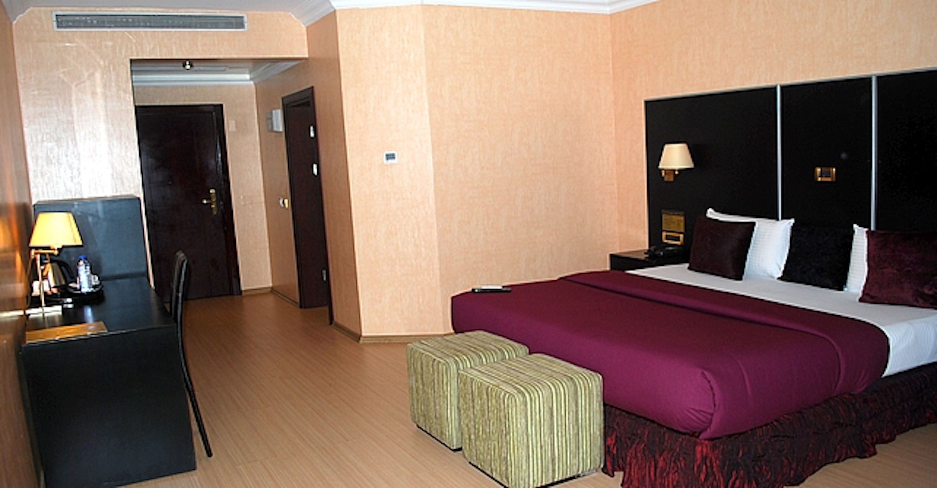 A hotel room with a bed, a desk, a chair, and a small table with a lamp.