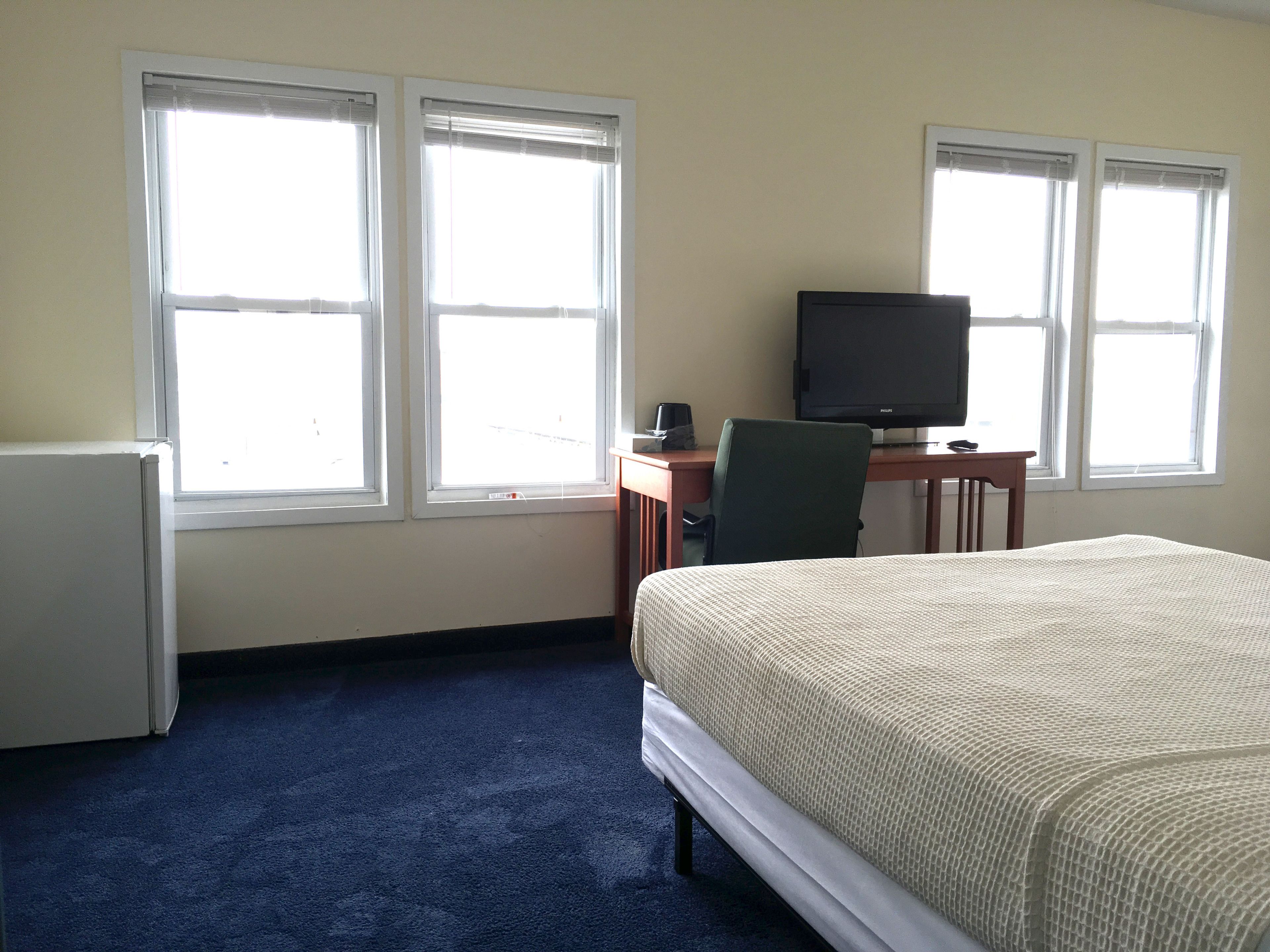 Una habitación de hotel con una cama, un escritorio con una computadora y dos ventanas.