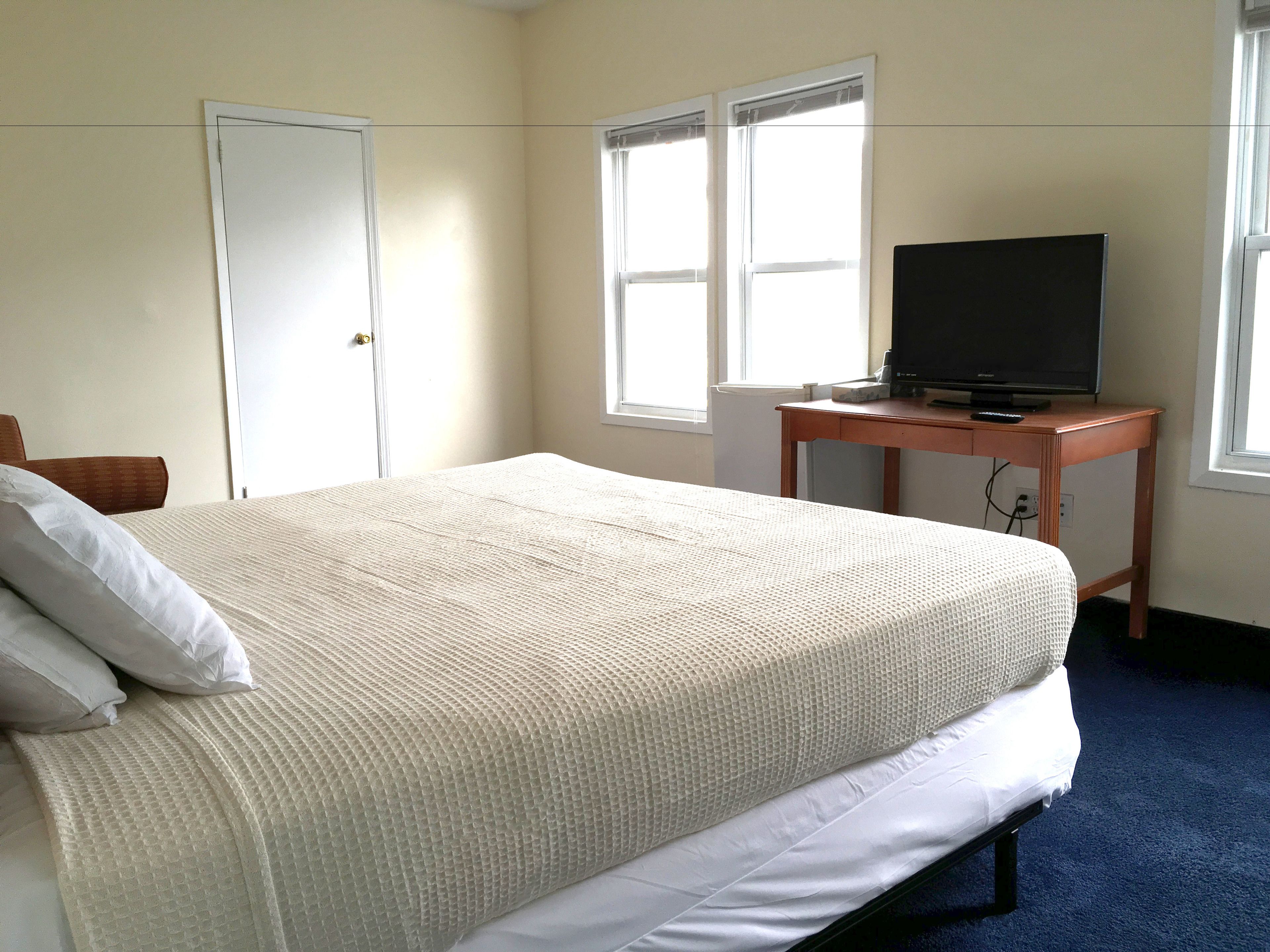 A bedroom with a bed, a television on a wooden table, and a door.