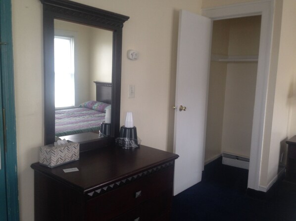 Habitación de hotel con un espejo grande, una cómoda, una cama con colcha colorida y una puerta blanca.