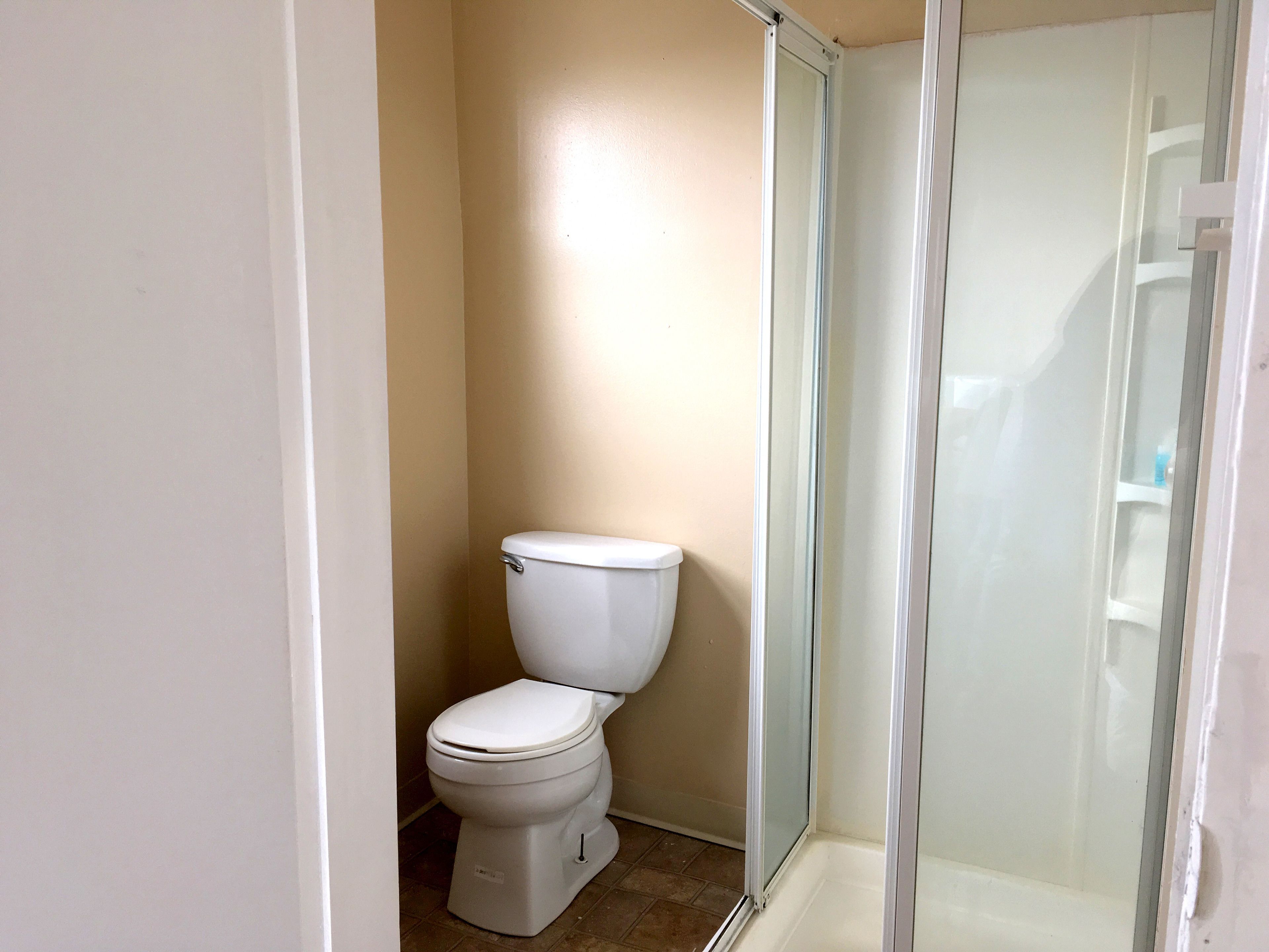 Une salle de bain comprenant des toilettes, un espace douche et un sol carrelé.