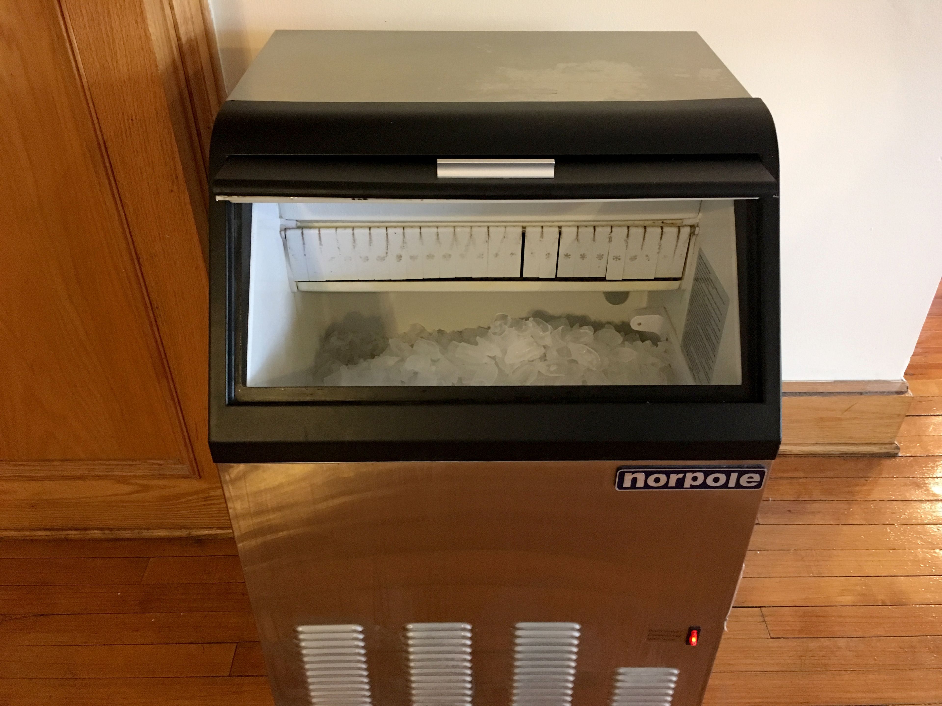 A Norpole ice maker with a glass front, located in a room with wooden flooring.