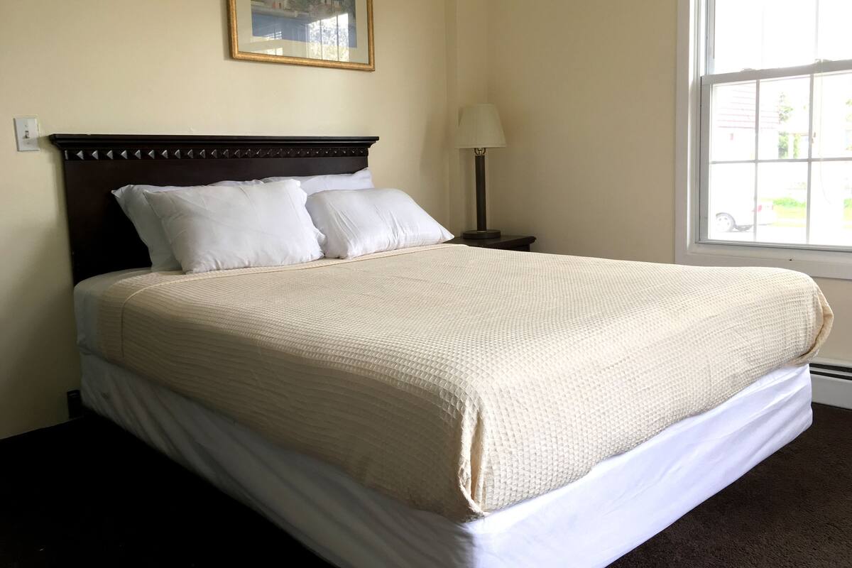 Una cama bien hecha con cabecera, una lámpara de noche y una ventana con vistas al exterior.