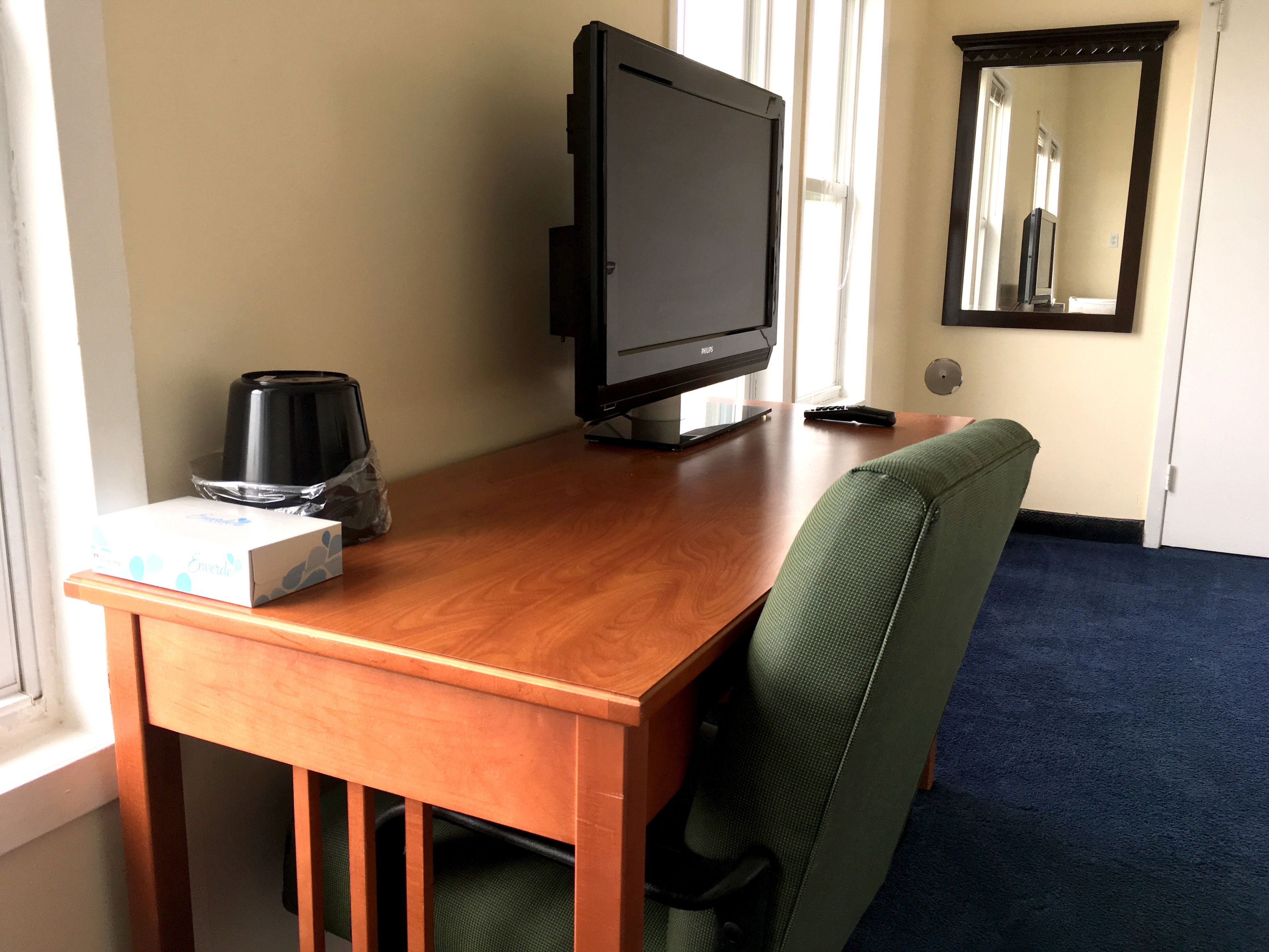 Een houten bureau met een televisie, een afstandsbediening en een koffiezetapparaat.