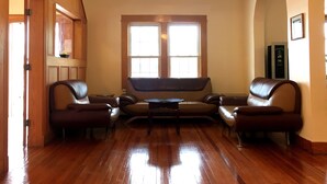 Un salón amplio con piso de madera, ventilador de techo y un ventanal grande.