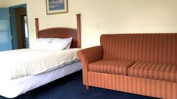 Habitación de hotel con una cama, un sofá marrón estampado, un cuadro en la pared y una alfombra azul.