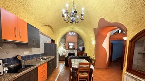 Una cocina con un arco de piedra, un comedor con mesa y sillas, y un televisor al fondo.