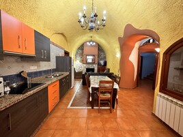 A kitchen with a stone archway, a dining area with a table and chairs, and a television in the background.