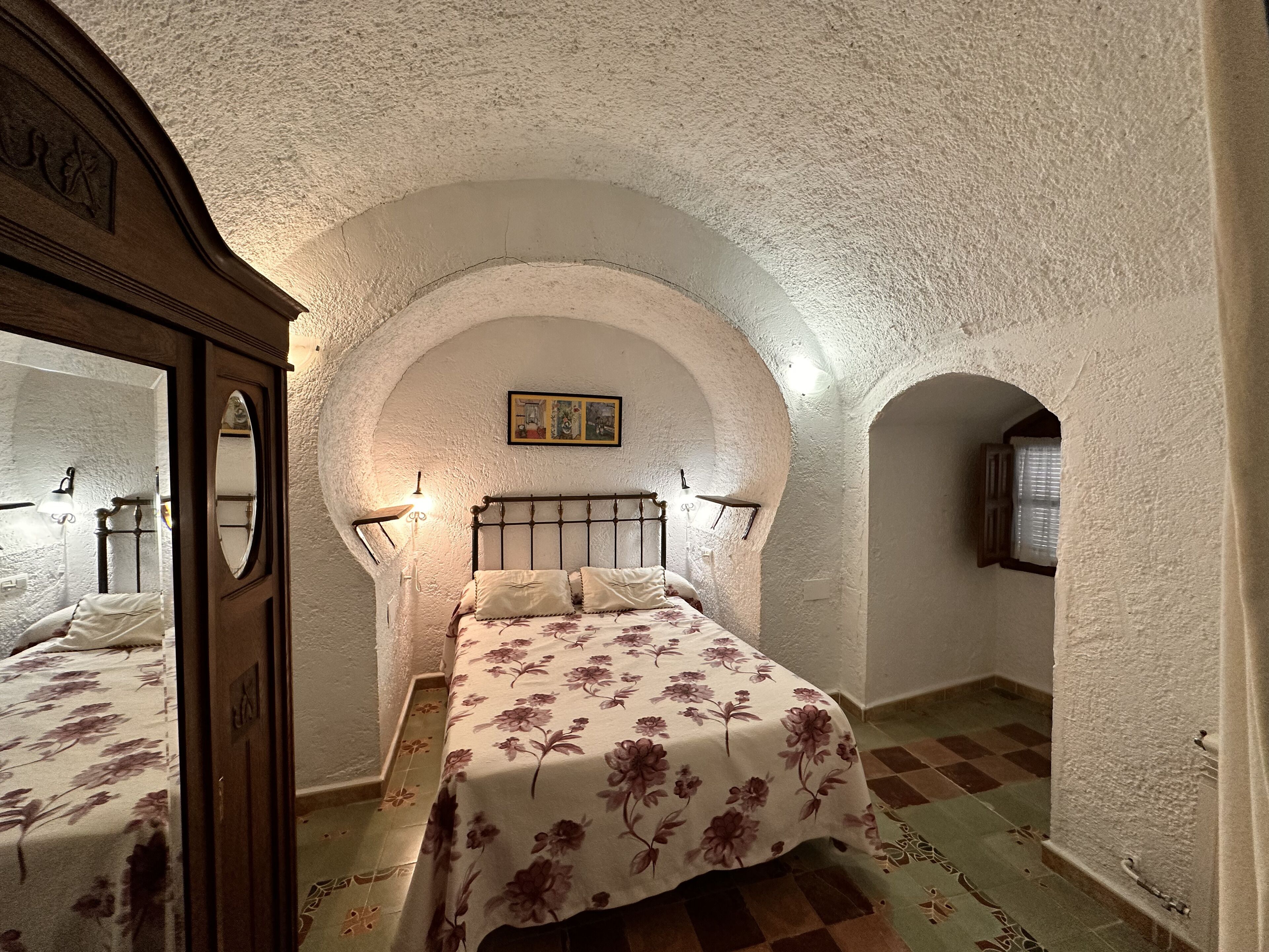 Un dormitorio con una cama bajo un techo abovedado, un armario de madera y un ventanal.