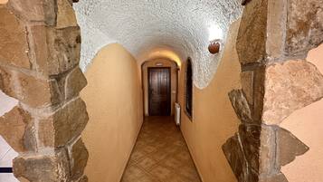 Un estrecho pasillo con paredes de piedra y suelo de baldosas, que conduce a una puerta de madera al final.