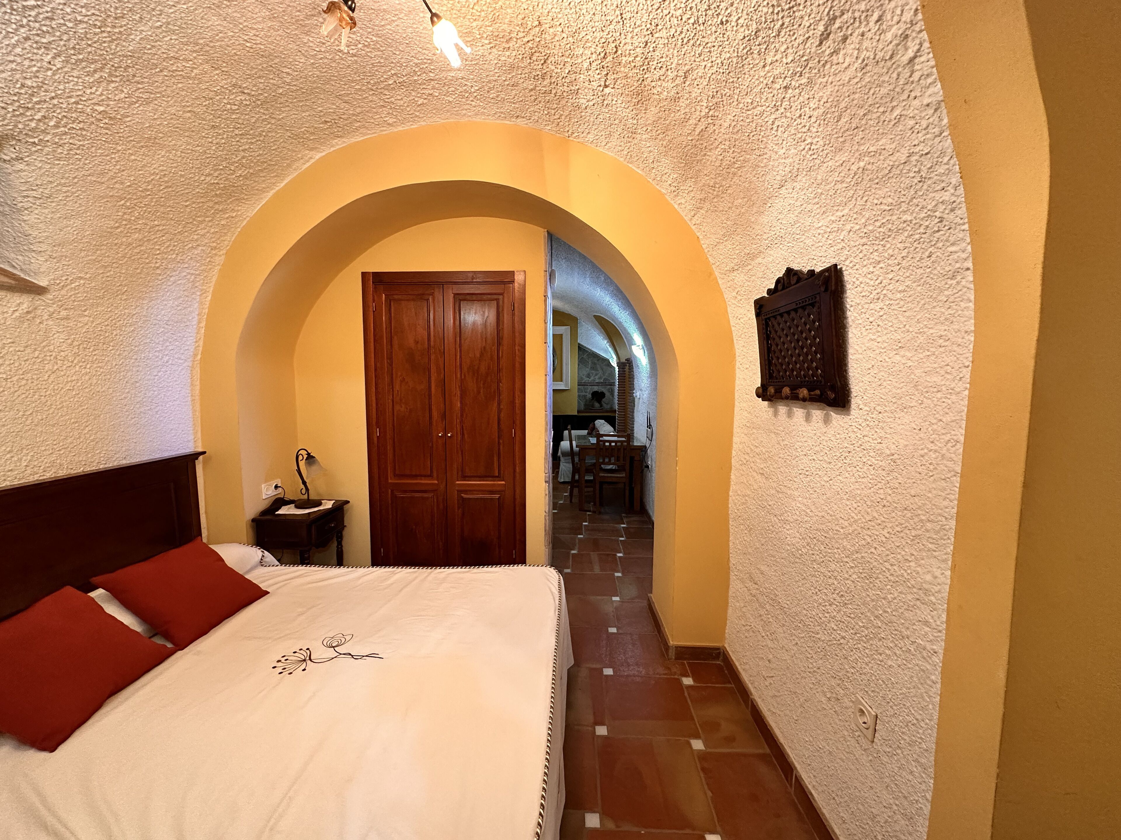 Una camera da letto con un letto, un comodino, una porta in legno e un corridoio ad arco che conduce a una sala da pranzo.