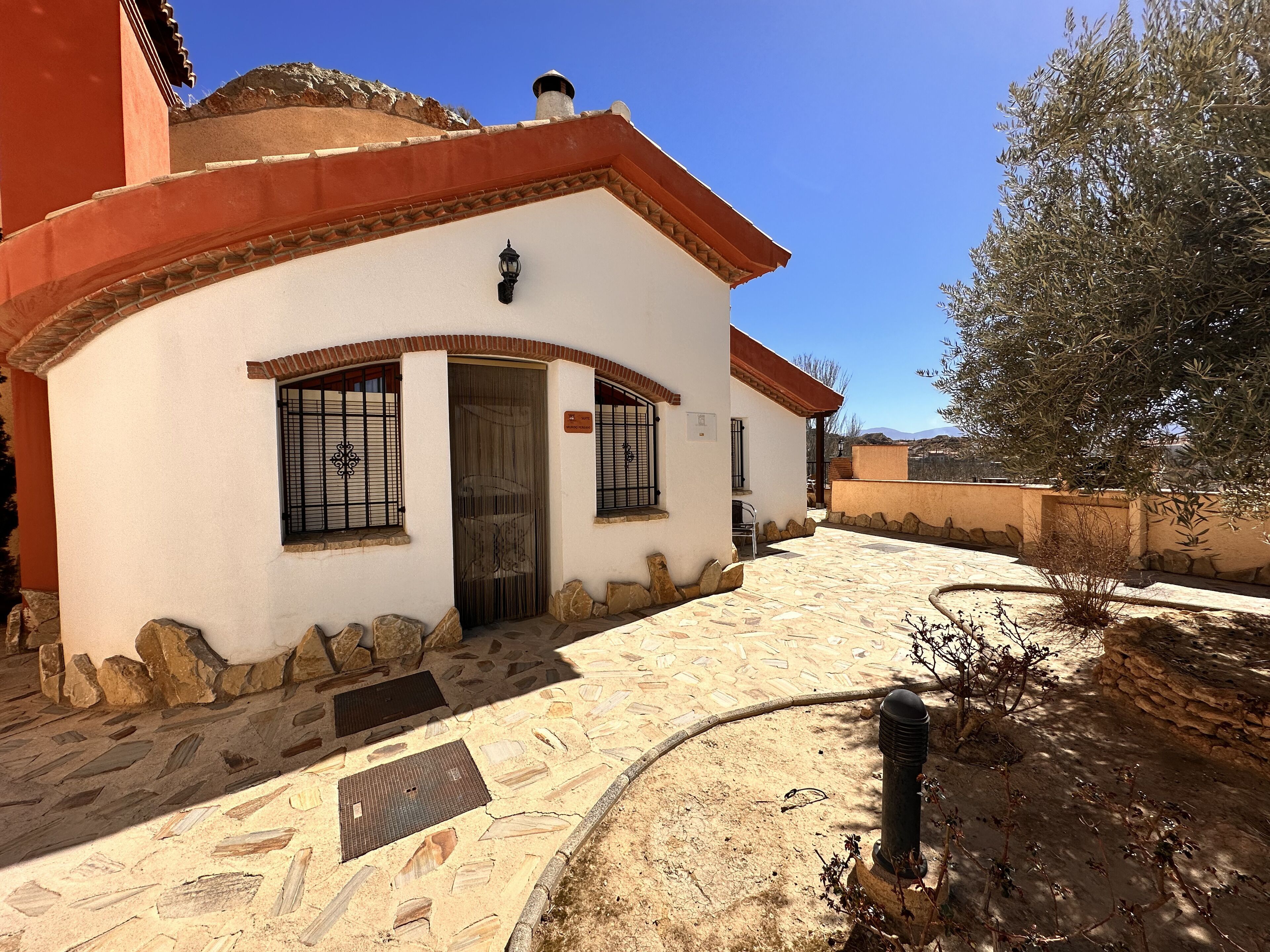Un edificio con fachada blanca, techo rojo y base de piedra. Tiene una puerta con ventana y un pequeño balcón.