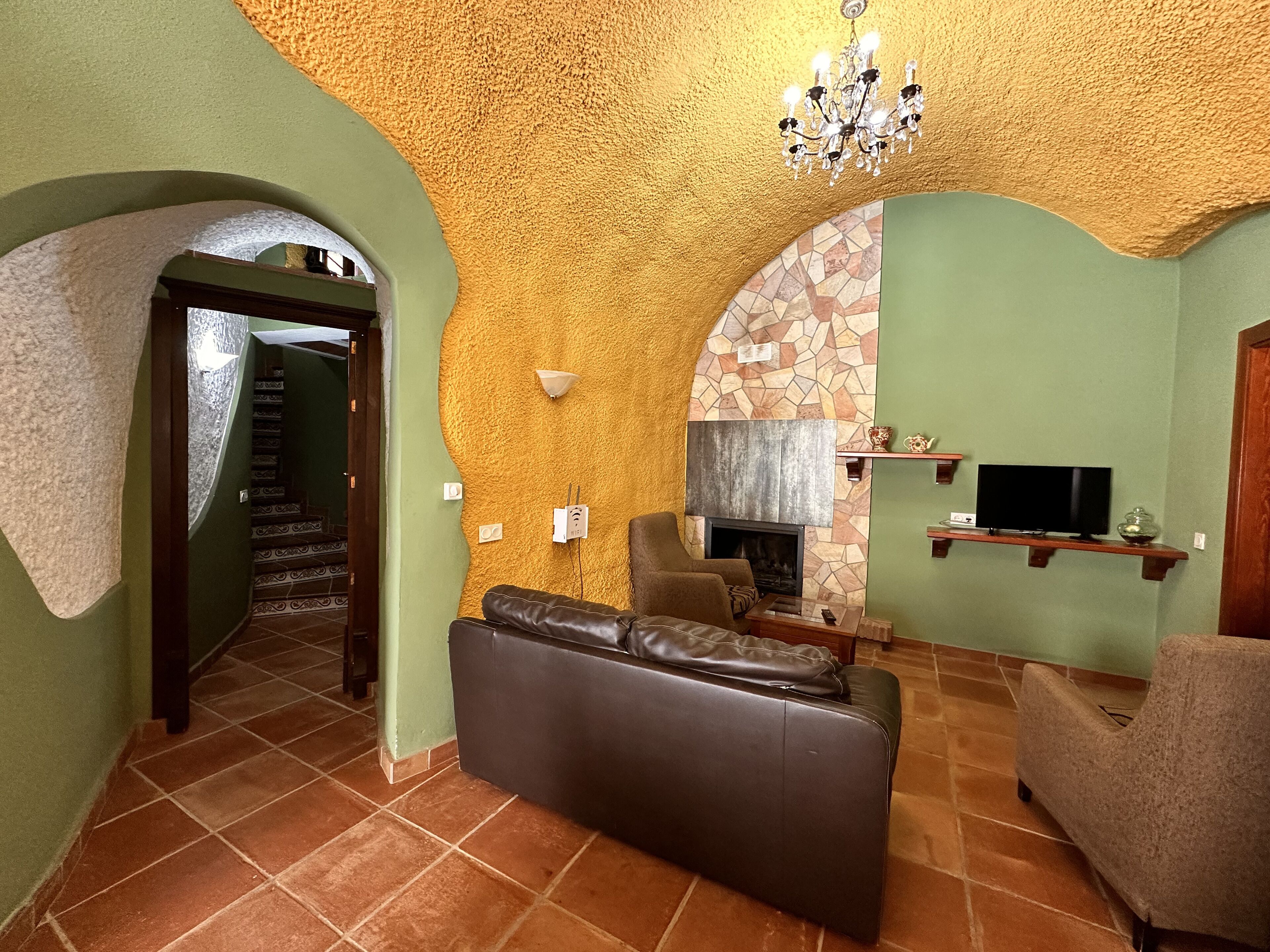 A living room with a fireplace, a sofa, a television, and a staircase leading to another room.