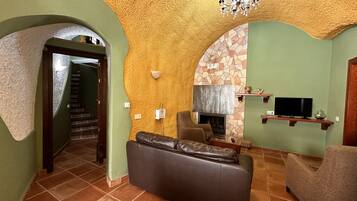 A living room with a fireplace, a sofa, a television, and a staircase leading to another room.