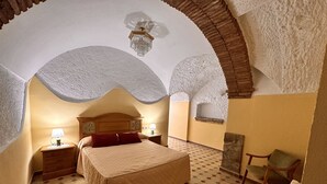 Un dormitorio con una cama grande, dos mesitas de noche con lámparas, una silla y una lámpara decorativa en el techo.