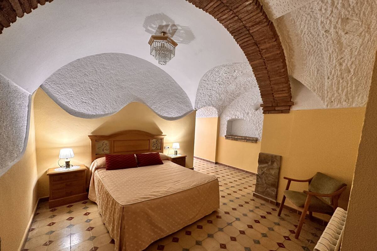 A bedroom with a large bed, two bedside tables with lamps, a chair, and a decorative ceiling light.