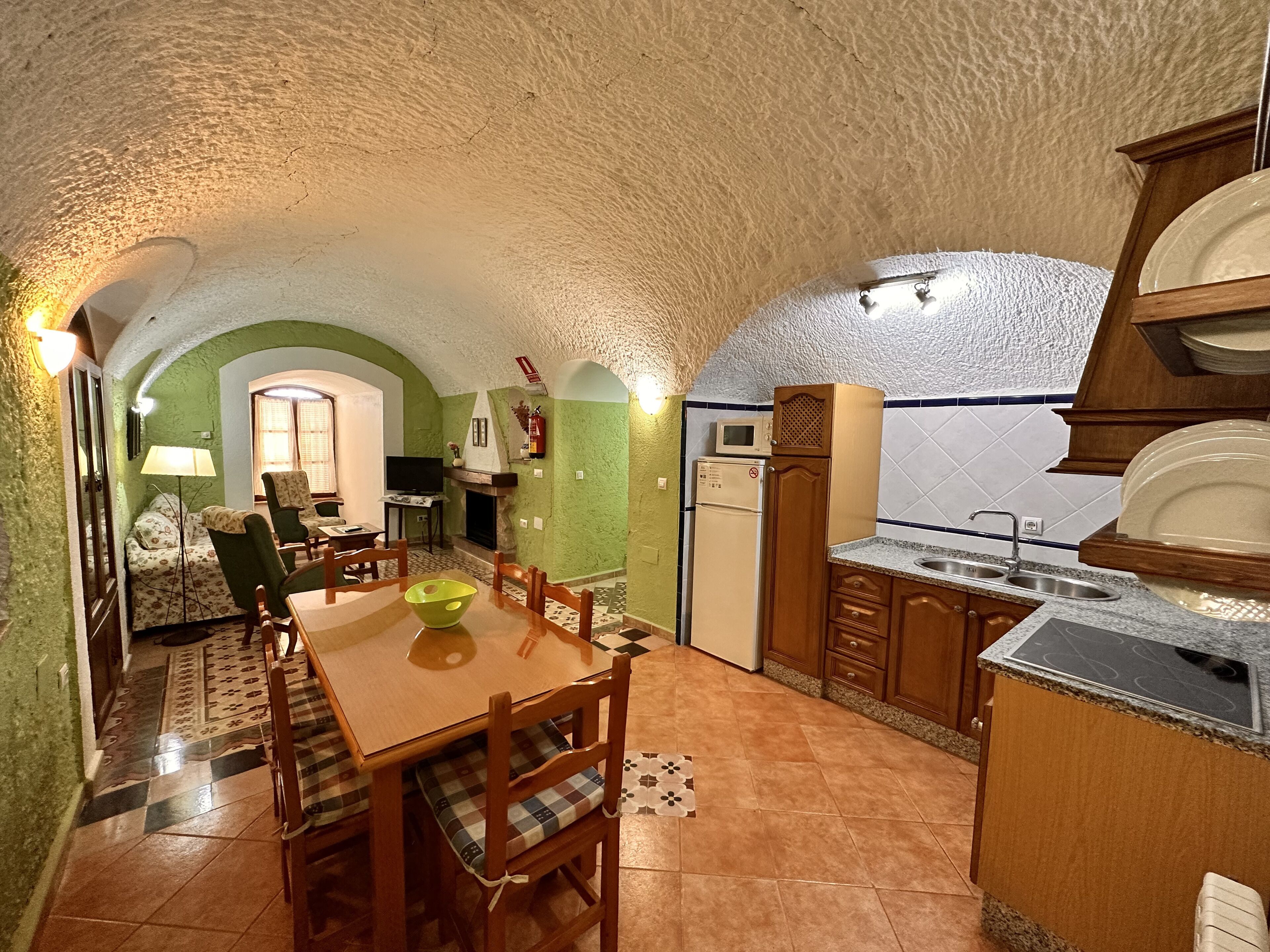 A compact kitchen with a dining area, featuring a stone arch ceiling, green walls, and a tiled floor.
