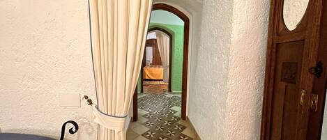 A corridor with patterned tiles, a wooden door, and a bed with a green wall in the background.