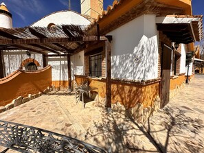 Un patio con suelo de piedra, un horno de ladrillo y una mesa de metal.